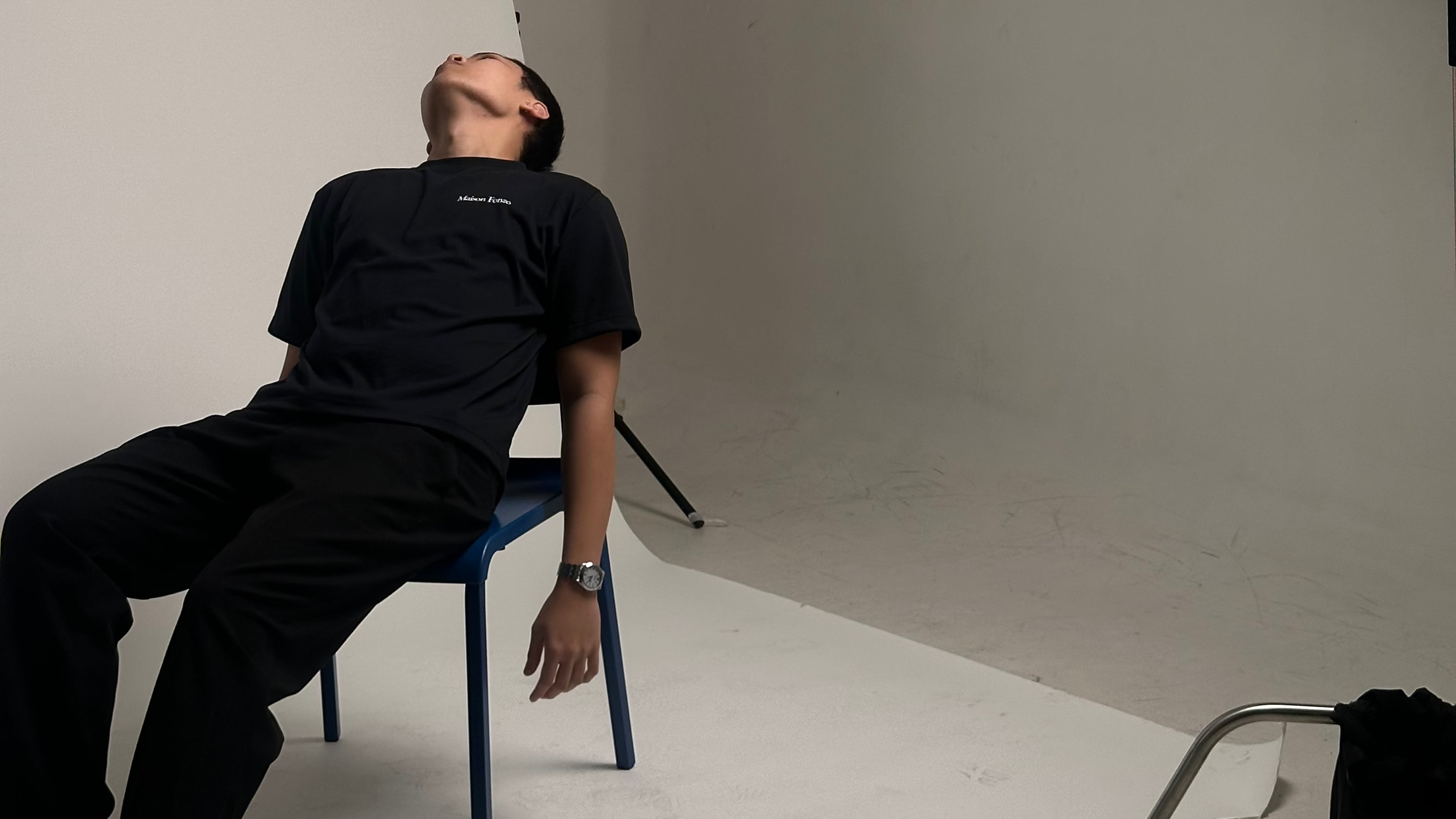 Person sitting on a chair in a studio with photography equipment, including a softbox light.
